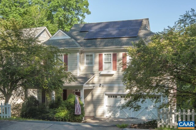 view of front of home featuring an attached garage, a shingled roof, fence, and solar panels