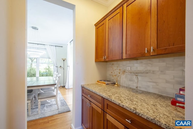 kitchen with light wood finished floors, light stone counters, brown cabinets, and decorative backsplash