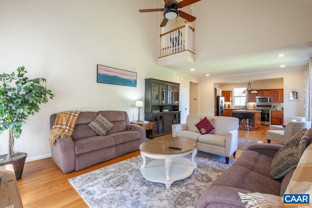 living area with baseboards, a ceiling fan, a high ceiling, light wood-type flooring, and recessed lighting