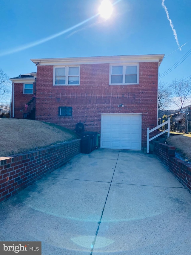 rear view of property featuring a garage, concrete driveway, brick siding, and fence