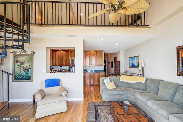 living room featuring light wood finished floors, a ceiling fan, baseboards, a high ceiling, and recessed lighting