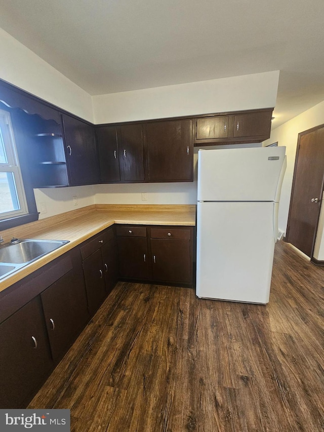 kitchen featuring light countertops, dark brown cabinets, dark wood-type flooring, and freestanding refrigerator