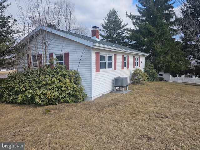 view of home's exterior with central AC, a yard, and a chimney