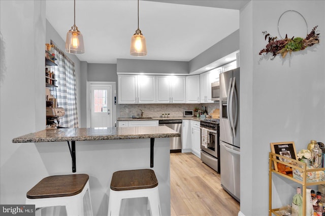 kitchen featuring decorative backsplash, appliances with stainless steel finishes, light stone counters, a peninsula, and white cabinetry