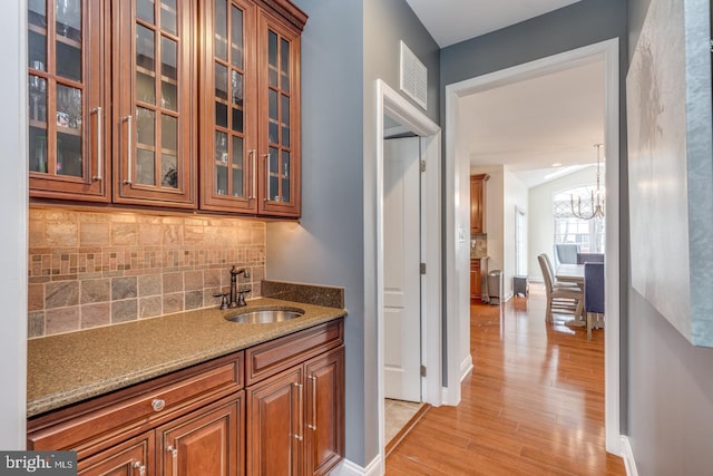 bar with baseboards, decorative backsplash, light wood-type flooring, a chandelier, and a sink