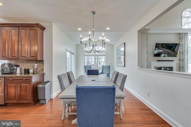 dining area with a healthy amount of sunlight, light wood-style floors, a chandelier, and vaulted ceiling