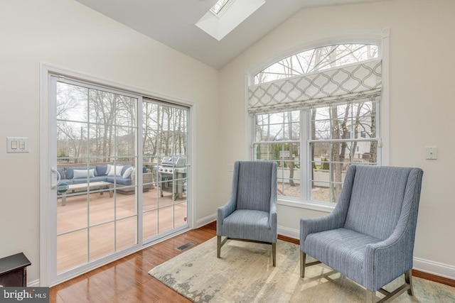 sitting room featuring lofted ceiling with skylight, wood finished floors, visible vents, and baseboards