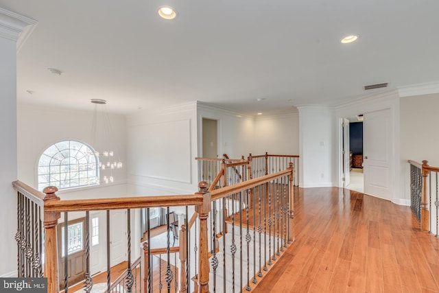 hallway with light wood finished floors, recessed lighting, visible vents, ornamental molding, and an upstairs landing