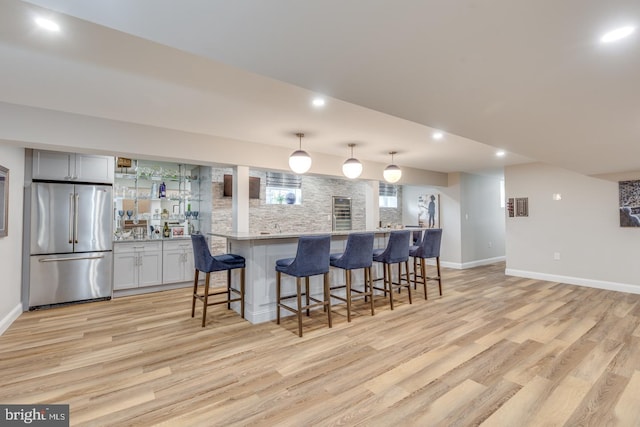 kitchen featuring tasteful backsplash, a breakfast bar area, freestanding refrigerator, and light wood-style floors