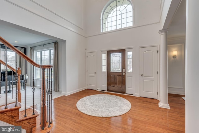 foyer entrance featuring stairs, light wood finished floors, baseboards, and ornate columns