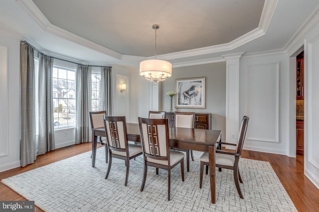 dining area with a tray ceiling, a chandelier, wood finished floors, and ornamental molding