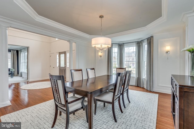 dining room with a tray ceiling, crown molding, decorative columns, light wood-style flooring, and baseboards