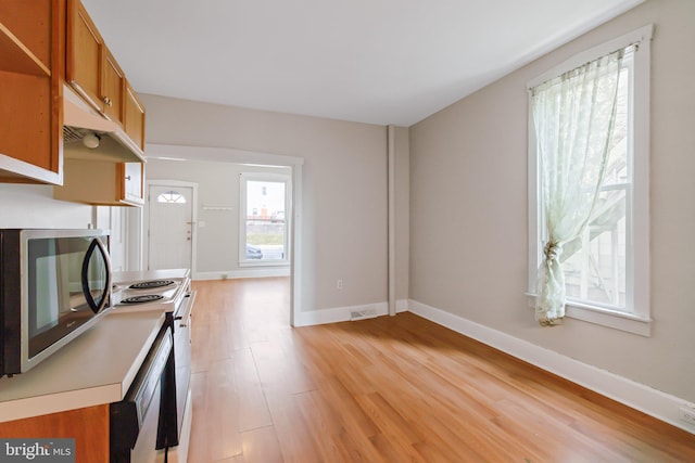 kitchen with brown cabinets, stainless steel microwave, white range with electric stovetop, light wood-style floors, and baseboards