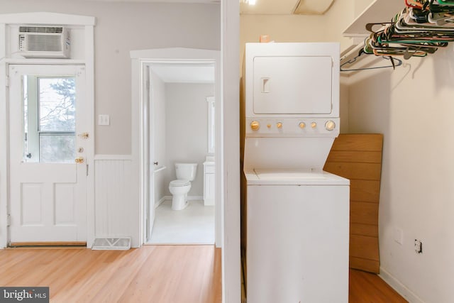 laundry area with visible vents, stacked washer and dryer, an AC wall unit, light wood-style floors, and laundry area