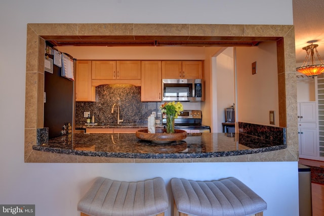 kitchen with a sink, a peninsula, appliances with stainless steel finishes, and backsplash