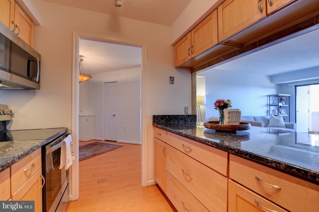 kitchen with light wood-style flooring, light brown cabinets, dark stone counters, and stainless steel appliances