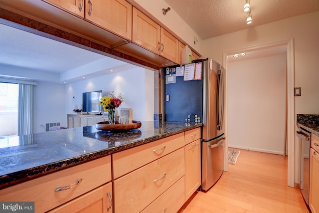 kitchen with appliances with stainless steel finishes, light wood-type flooring, a textured ceiling, and dark stone countertops