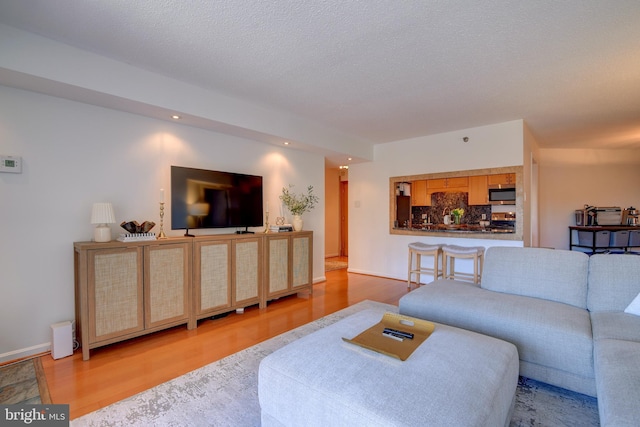 living area featuring a textured ceiling, recessed lighting, wood finished floors, and baseboards