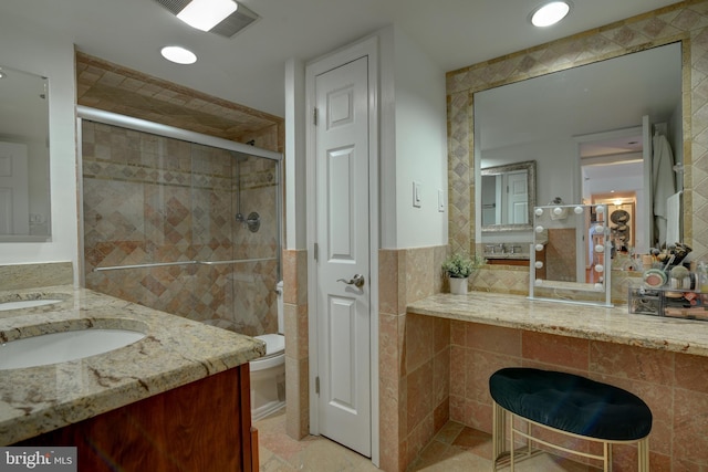 bathroom featuring toilet, visible vents, vanity, tile walls, and a stall shower