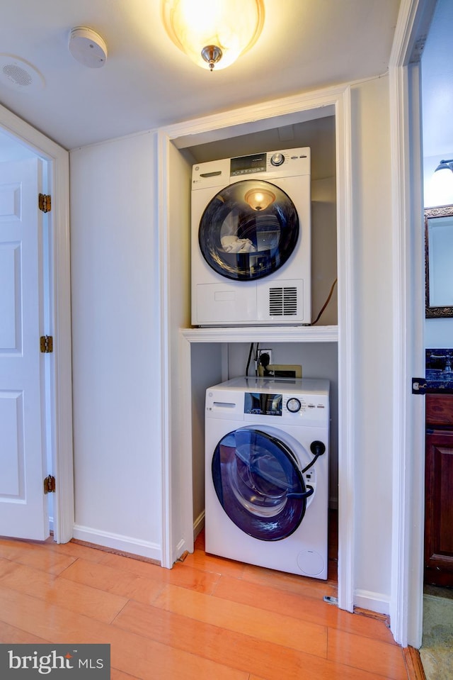 clothes washing area featuring laundry area, light wood-style flooring, stacked washer and clothes dryer, and baseboards