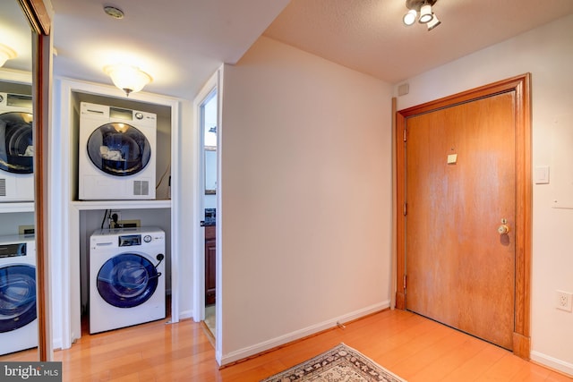 washroom with baseboards, stacked washer and dryer, laundry area, and light wood-style floors