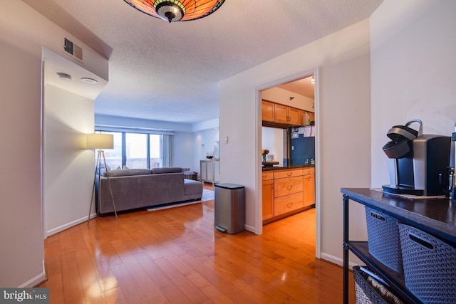 living area with light wood finished floors, baseboards, visible vents, and a textured ceiling