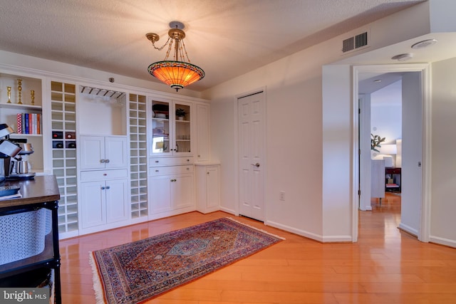 dining room featuring a textured ceiling, light wood-style flooring, visible vents, and baseboards