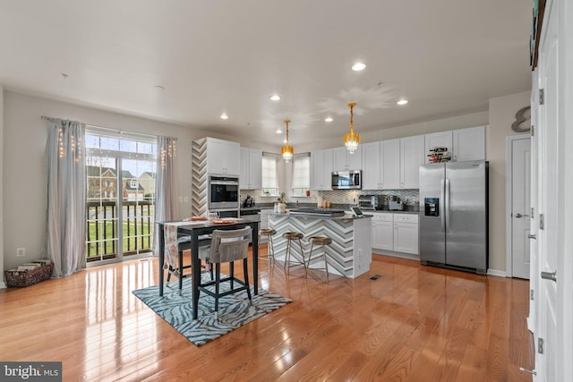 kitchen featuring white cabinets, appliances with stainless steel finishes, light wood-type flooring, backsplash, and dark countertops