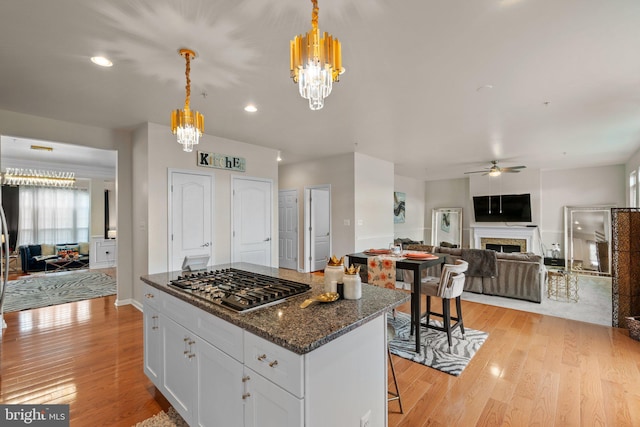 kitchen featuring a fireplace, stainless steel gas cooktop, light wood-style floors, open floor plan, and white cabinets