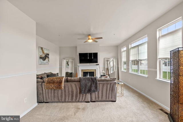 living room with light carpet, ceiling fan, a fireplace, and baseboards