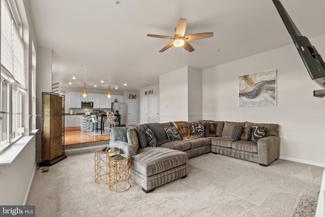 living area featuring light carpet, ceiling fan, and baseboards