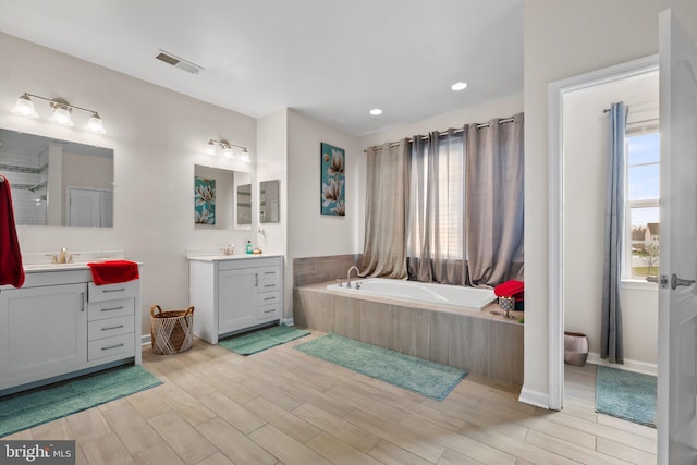 full bath featuring a sink, wood finished floors, two vanities, visible vents, and a bath