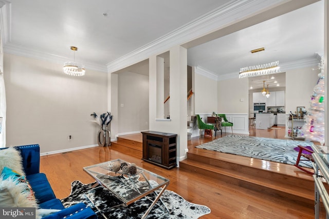 living area with a chandelier, light wood-type flooring, crown molding, and stairway