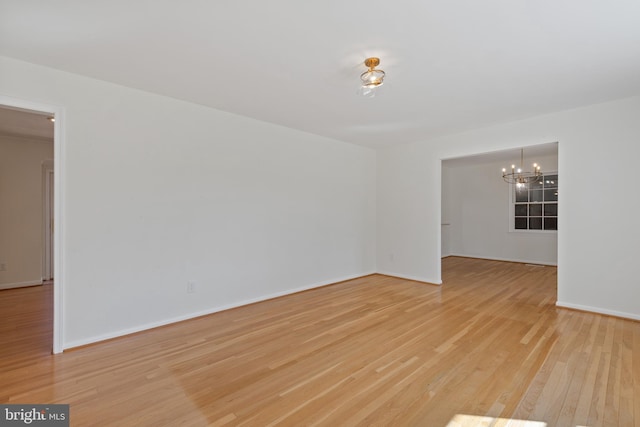 empty room featuring a chandelier, light wood-type flooring, and baseboards