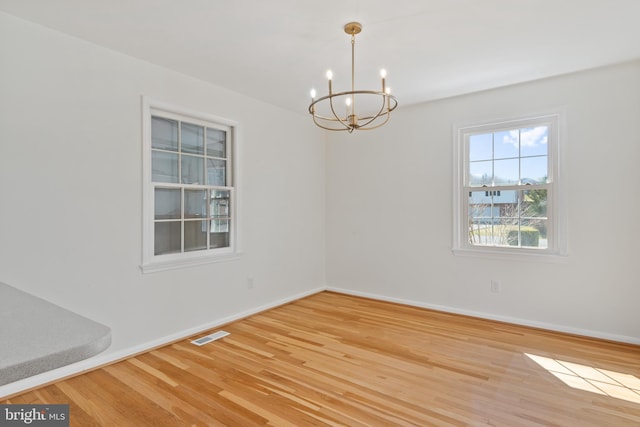 spare room with a notable chandelier, visible vents, baseboards, and wood finished floors