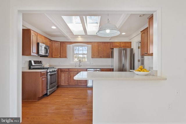 kitchen featuring stainless steel appliances, a peninsula, light wood-style flooring, and light countertops