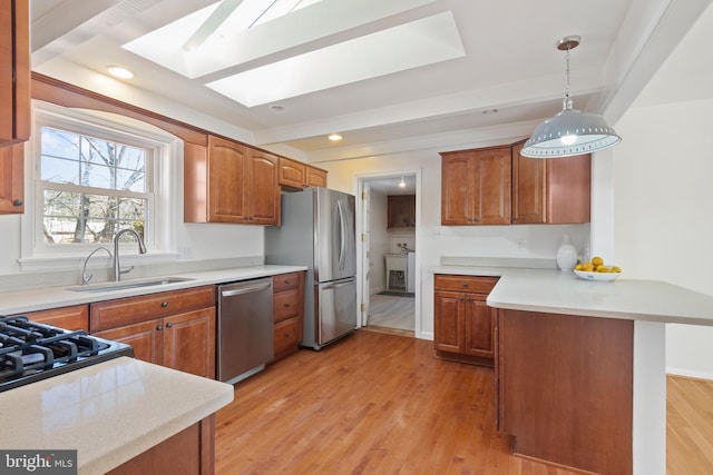 kitchen featuring a sink, a peninsula, appliances with stainless steel finishes, a skylight, and light countertops