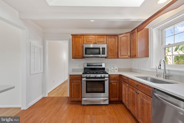 kitchen with a sink, stainless steel appliances, light countertops, and light wood finished floors