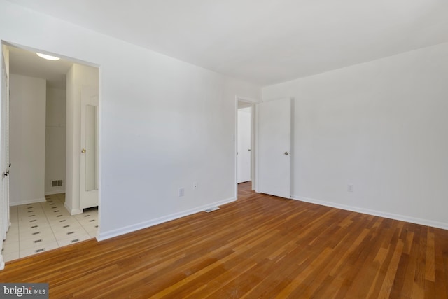 spare room featuring light wood-type flooring, baseboards, and visible vents