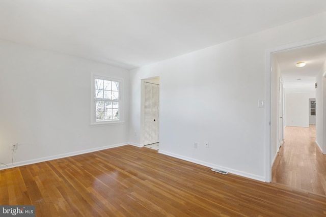 spare room with wood finished floors, visible vents, and baseboards