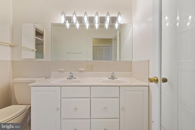 full bath with tile walls, toilet, double vanity, and a sink