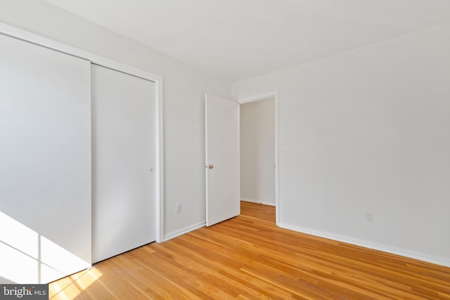 unfurnished bedroom with light wood-style flooring, baseboards, and a closet