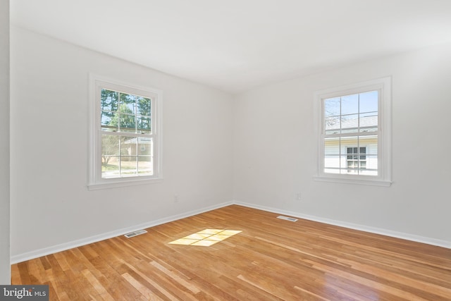 empty room with light wood-type flooring, visible vents, and baseboards