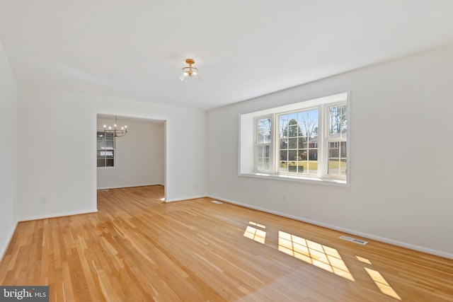 unfurnished room featuring baseboards, visible vents, light wood finished floors, and a chandelier