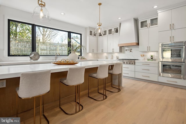 kitchen with light wood finished floors, tasteful backsplash, appliances with stainless steel finishes, custom exhaust hood, and light countertops