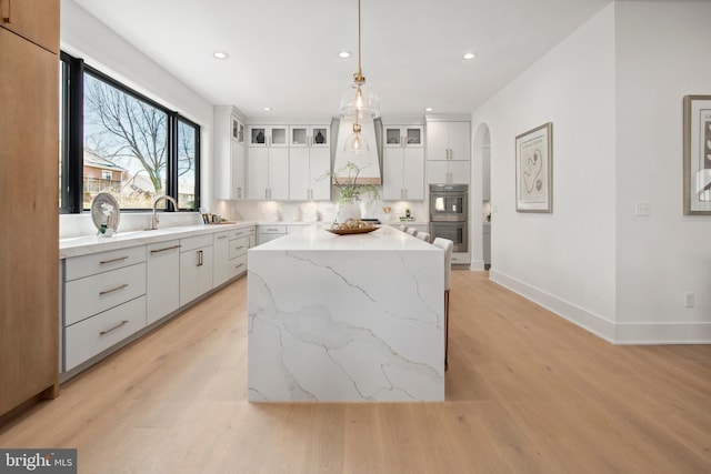 kitchen featuring arched walkways, light wood finished floors, decorative backsplash, double oven, and white cabinetry