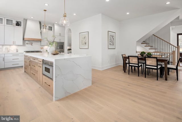 kitchen with white cabinets, glass insert cabinets, a center island, light wood-type flooring, and premium range hood