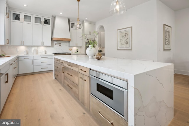 kitchen with stainless steel microwave, a center island, custom exhaust hood, light wood-type flooring, and backsplash