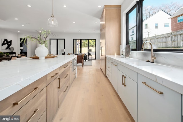 kitchen featuring light stone countertops, light wood-style flooring, a sink, and recessed lighting