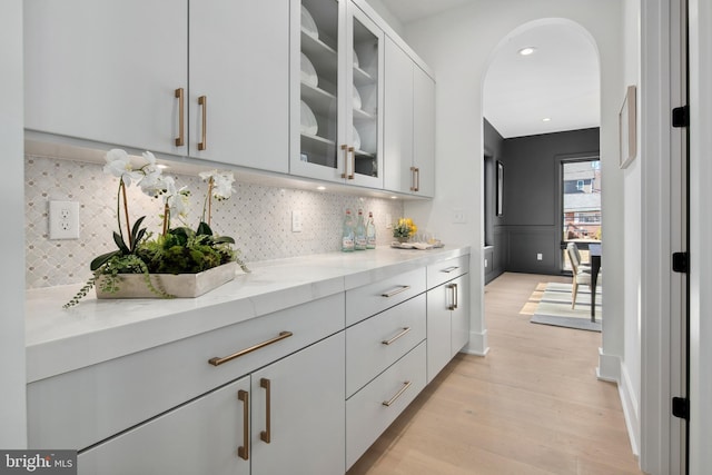 interior space featuring arched walkways, light wood-type flooring, decorative backsplash, and light stone countertops